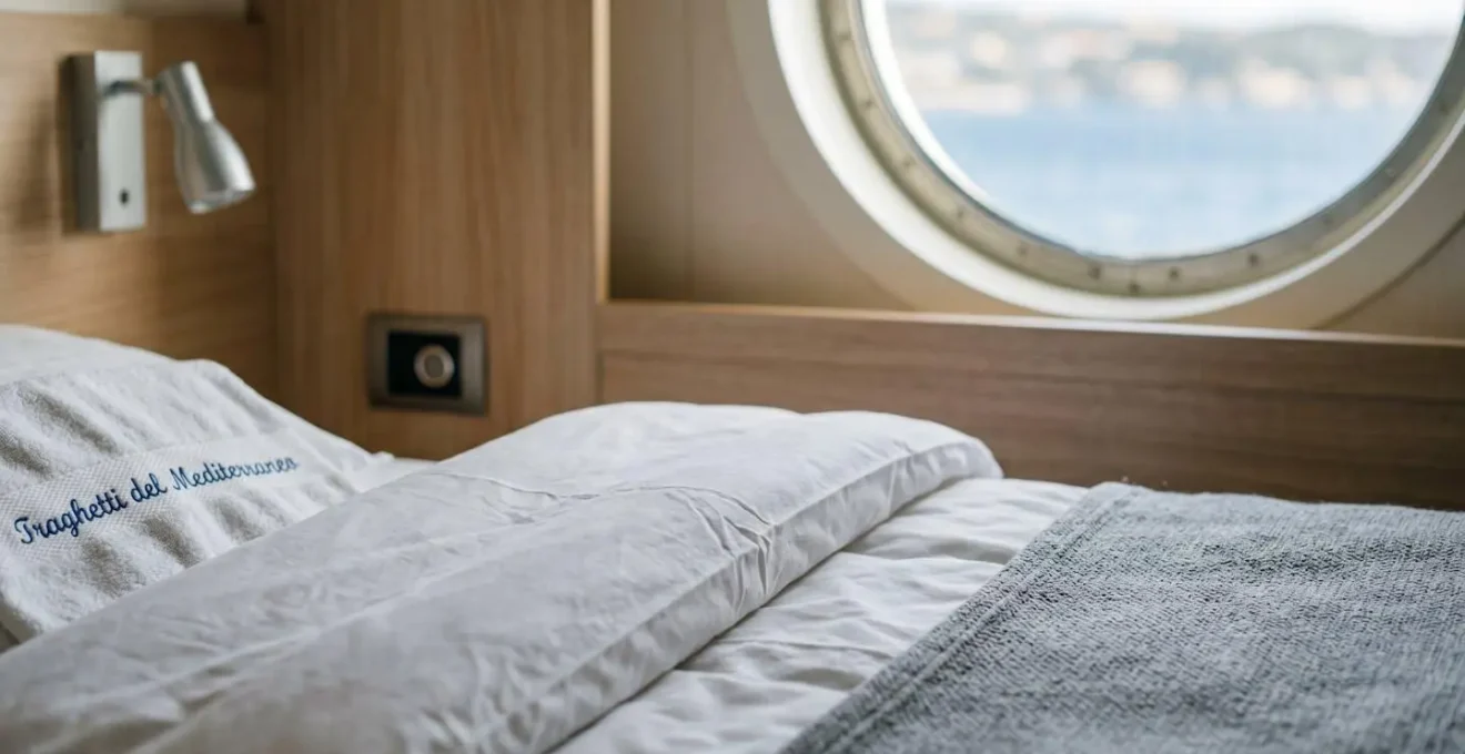 Dettaglio ravvicinato di una cabina di traghetto moderna con letto pulito e oblò sullo sfondo sfocato
